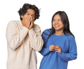 Young interracial couple in studio laughing about something, covering mouth with hands.
