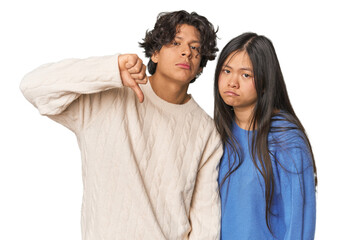 Young interracial couple in studio showing a dislike gesture, thumbs down. Disagreement concept.