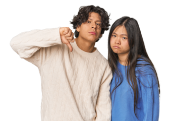 Young interracial couple in studio showing a dislike gesture, thumbs down. Disagreement concept.