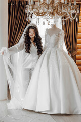 Fototapeta premium A bride is standing in front of a wedding dress, which is displayed on a mannequin. The dress is white and has a long train. The bride is wearing a veil and a crown