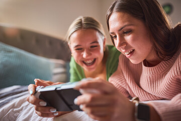 Two Teenage Girls At Home In Bedroom Together Playing On Handheld Computer Gaming Device Together © Monkey Business