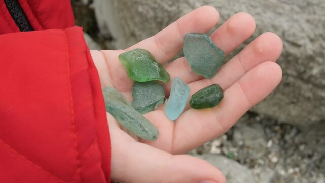 The child holds transparent sea stones in his hands. The close-up captures beauty of the colored stones in children's hands, perfect for the theme of children's curiosity, exploration and discovery.