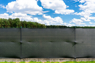 Anthracite-colored masking net placed on a mesh fence, visible garden and lawn.