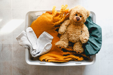 Ein Wäschekorb mit Schmutzwäsche und einem braunen Teddybär. Draufsicht, Fliesenboden.
