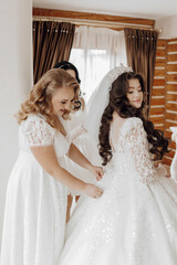 A woman in a white dress is getting her hair done by another woman. The two women are standing in front of a window