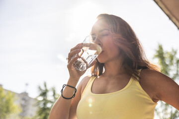 Dehydrated woman drinks clean water from a glass to replenish fluids during hot summer days