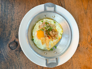 Pan-fried eggs topped with pork sausage and pepper on a stainless steel plate.