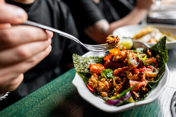 Close-up of a person enjoying a colorful Asian-style dish with vegetables and rice