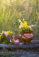wiccan Goddess Candlestick, witch Copper cauldron with flowers on meadow, natural background. herb...