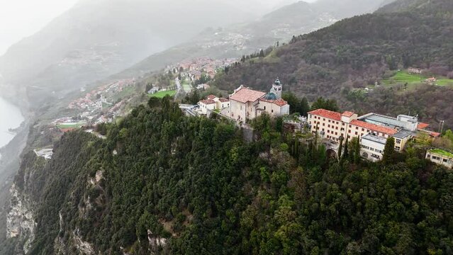 Aerial footage over Tignale Montecastello shrine on Lake Garda in Lombardy, Italy. Catholic church on a mountain surrounded by the Alps