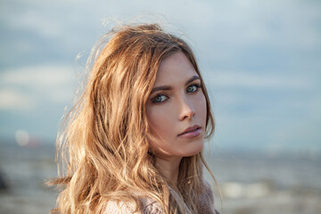 Beautiful young adult woman with natural make-up and long wavy brown hair on blue sea beach outdoor portrait