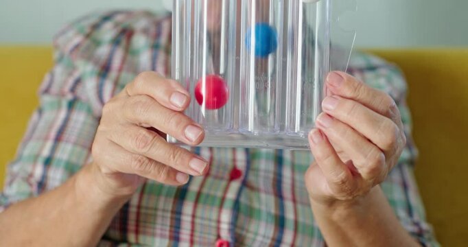 An elderly woman blows into a special device - spirometer to train her lungs and test lung capacity. Close-up shot