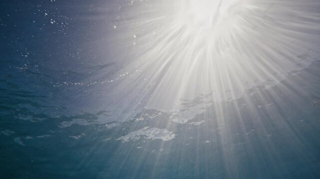 Light rays sparkle and spread out in dazzling rows through ocean surface, underwater view in slow motion for nature background