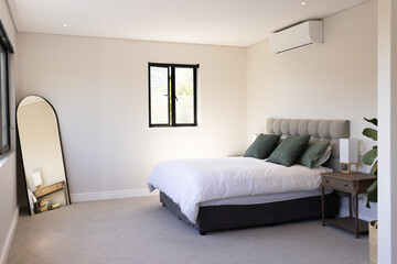 Fototapeta premium Modern bedroom with cozy bed, green pillows, and large mirror by window, copy space