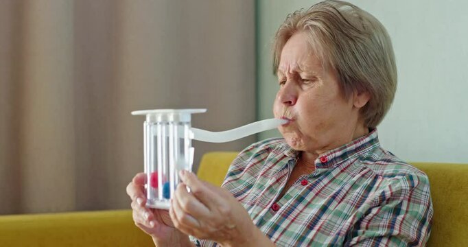An elderly woman blows into a special device - spirometer to train her lungs and test lung capacity