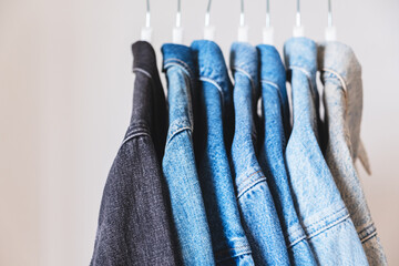 Many denim trucker jackets on hangers. Different shades of jean textile colors.