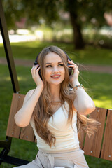 Beautiful young girl listening to music on headphones sitting on a bench on a sunny day. Music.