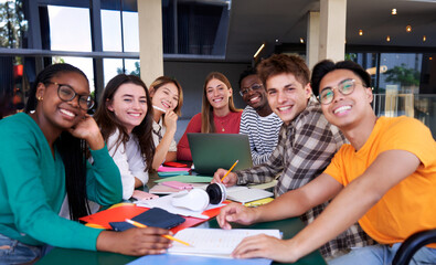 Cheerful portrait of a large multiracial group of university students sitting in a table at campus looking at camera smiling, studying together after classes.