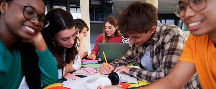 Large multiracial group of university students sitting in a table at campus studying together after classes, concentrated doing homework. - Powered by Adobe
