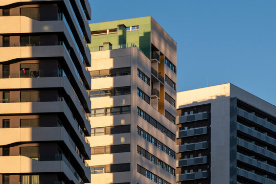 This image showcases modern high-rise buildings with geometric designs and contemporary architectural styles, bathed in warm light and set against a clear blue sky in Barcelona Spain