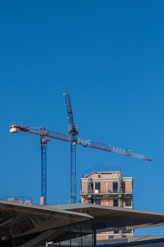 Gigantic cranes towering over a construction site against a clear blue sky, showcasing human engineering and the process of building modern urban structures within a cityscape.