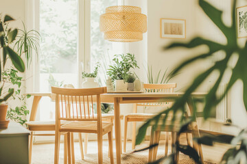 Fototapeta premium A Scandinavian dining room with white walls, light wood furniture, and green plants.