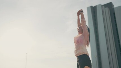A woman is standing outside in front of a tall building. She is wearing a pink jacket and black shorts. She is holding a cell phone in her hand