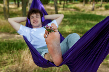 A young guy with curly hair is relaxing on a hammock on a hot summer day.