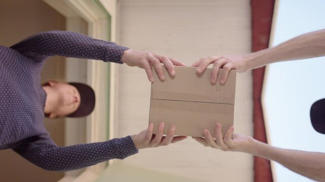 Home owner at door takes delivery of small carton box, low upward view