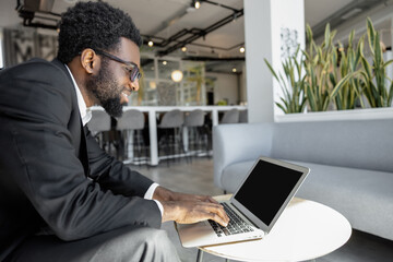 Dark-skinned confident businessman working on the laptop and looking busy