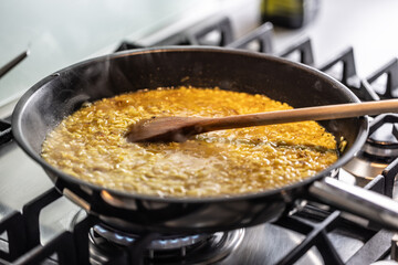 Preparation of saffron risotto in a pan on a gas stove