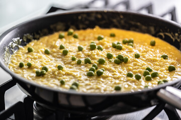 Saffron risotto with peas cooked in a pan on a gas stove