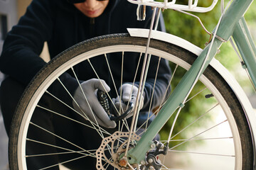 Thief in black unlocking the lock on the bike and trying to steal it