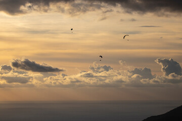 Paragliders gliding in the backlight in Ölüdeniz with the light filtering through the clouds