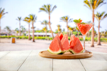 Watermelon slices cocktail in glass on wooden table top and blur background of tropical beach and blue sky. Empty advertising copy space for products and food.