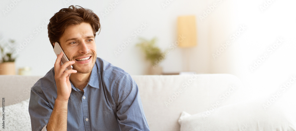 Poster a man sits on a couch while talking on his phone, smiling and looking to his left.