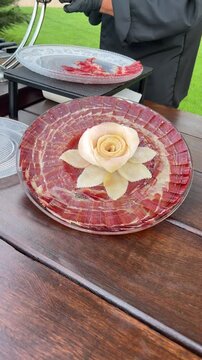 A plate of meat with a rose on it. The rose is made out of apples and is placed on top of the meat