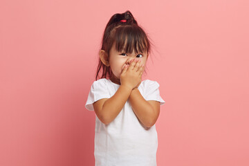Little Asian girl covers her mouth with her hand with her eyes wide open in shame, said something...