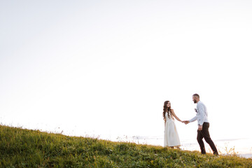 A couple is walking on a grassy hillside, hand in hand. The scene is peaceful and romantic, with the couple enjoying each other's company in a beautiful natural setting