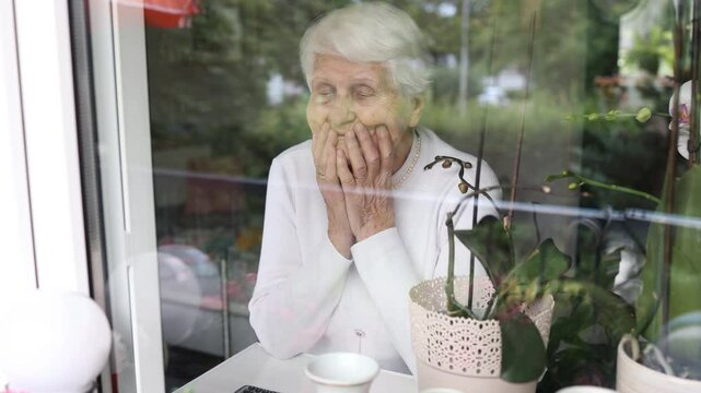 Lonely elderly woman looking out the window, waiting for someone to visit her