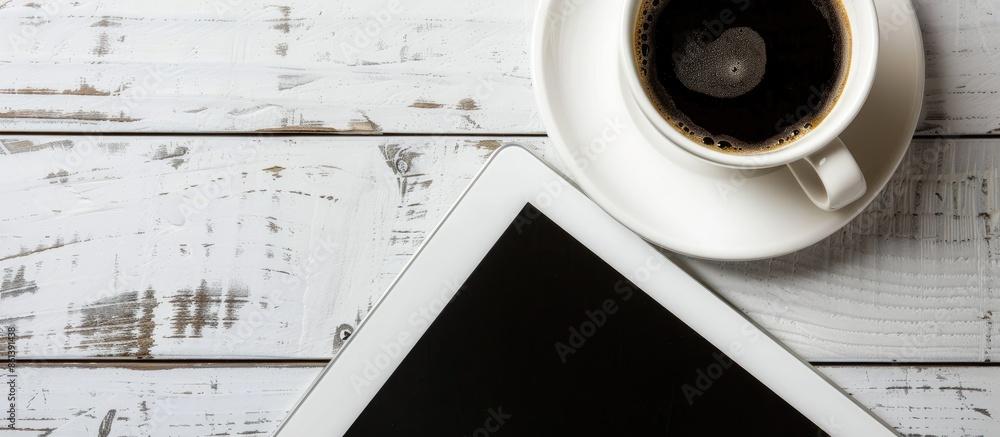 Aufkleber Top view of a computer tablet with a black screen placed beside a cup of coffee on a white table, featuring a close-up shot and ample copy space image.