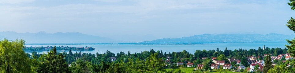 Germany, Lindau, XXL aerial panorama view above lindau island, bad schachen tower, lighthouse, city, tree tops and silent lake water early morning after sunrise, foggy view to swiss alps