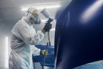 Male Industrial worker sprays paint using airbrush gun on part of car wears in protective mask and...