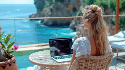 A woman sits coding on her laptop by a poolside with an expansive ocean view, enveloped by plants and flowers, showcasing a peaceful and focused work setting.