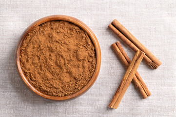 Ceylon cinnamon powder in a wooden bowl on linen. Ground bark of Ceylon cinnamon, Cinnamomum verum, and dried whole bark strips on the right. Used mainly as aromatic condiment and flavouring additive.