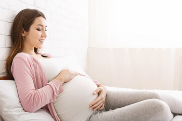 Active unborn baby pushing his mom, pregnant lady enjoying her pregnancy, lying in bed at home, copy space