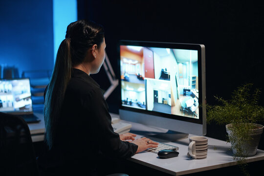 Rear view of woman typing on computer and watching on cameras in security room