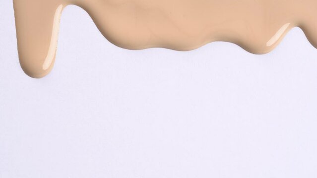 Foundation cream for face, BB cream, CC cream or concealer pouring on white background, macro shot. Cosmetic liquid foundation, or cream beige color smudge flowing down on a white surface.