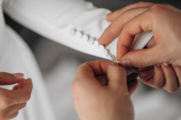 A woman is helping another woman with her dress. The woman is wearing a white dress and the other...