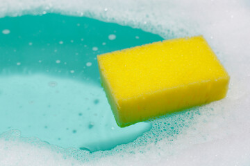 Yellow sponge floating on blue water with soap foam